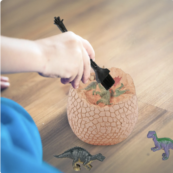Hand carefully brushing soil off a dinosaur figure inside the Jumbo Dinosaur Dig Egg.